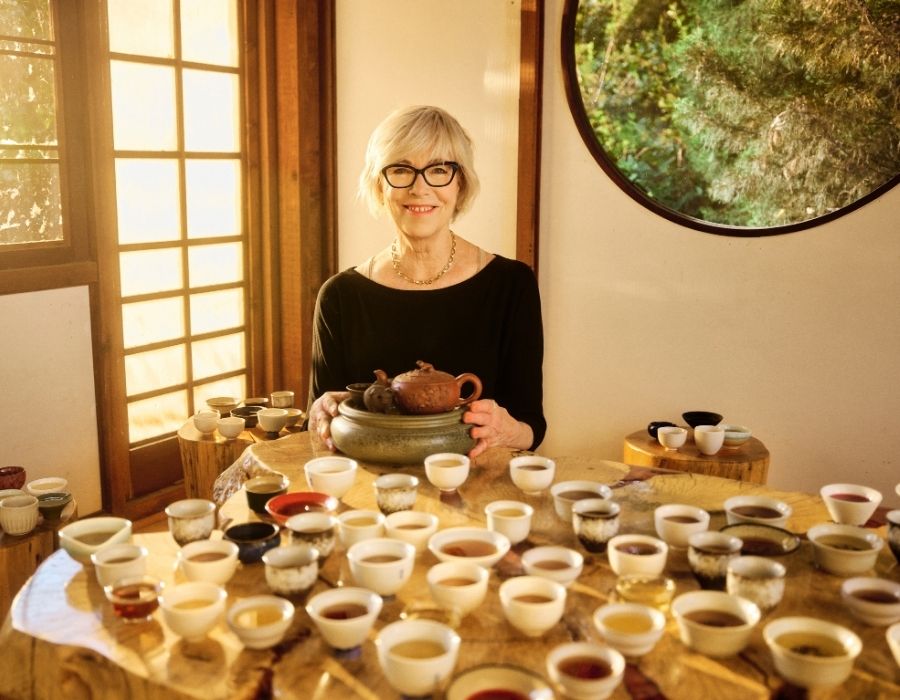 a woman sits behind a table with 101 tea cups on it