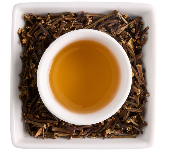 A top-down view of a small white teacup filled with ceylon cinnamon tea on a white background.
