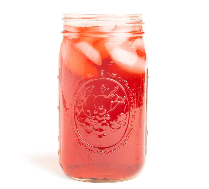 Bright red brewed Summer Solstice herbal iced tea served in a mason jar with ice, made from hibiscus, lemongrass, and goji berry.
